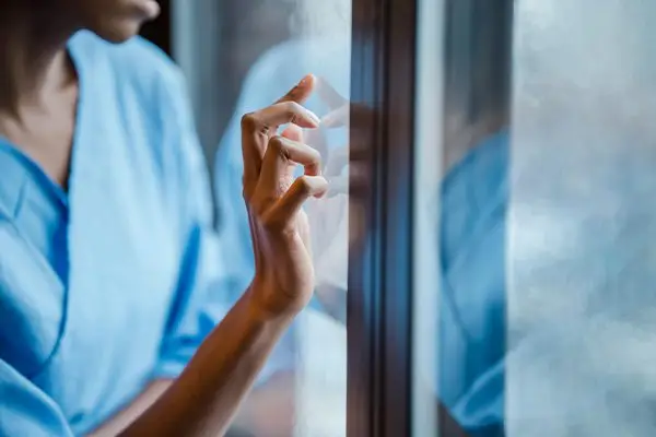 Person anxiously touching window while looking outside in deep thought