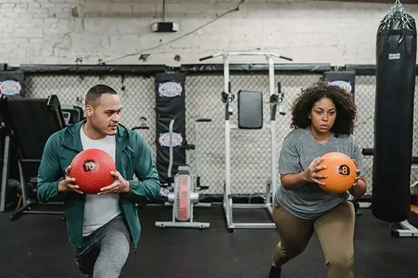 Man and woman performing strength training with medicine balls in a gym as part of a fitness and health program.