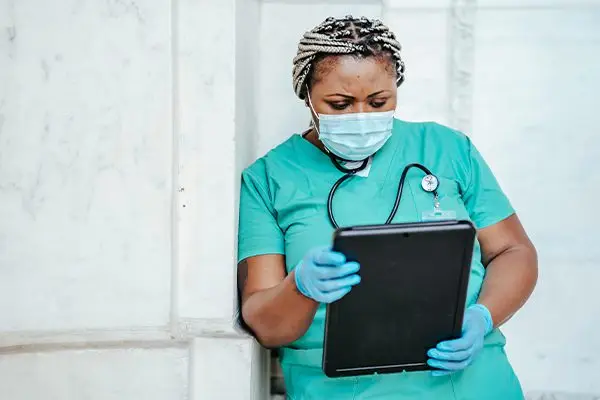Female healthcare professional in scrubs reviewing patient data on a digital tablet