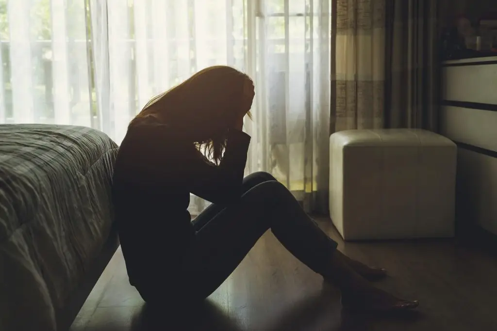 Woman sitting on the floor in a dark room with head in hands, feeling overwhelmed