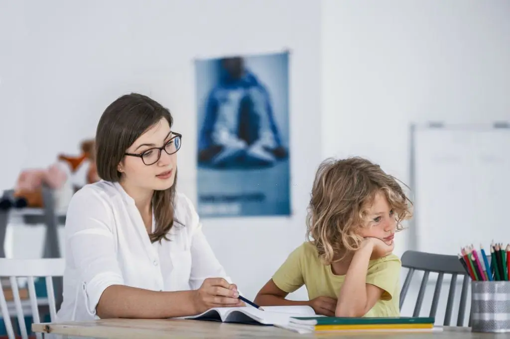 Female therapist working with a distracted young child during a behavioral consultation in a bright, child-friendly clinic.