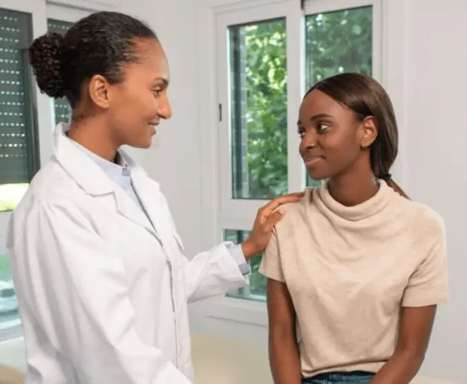 Female doctor gently comforting a young woman during a women's health consultation in a bright clinic room.